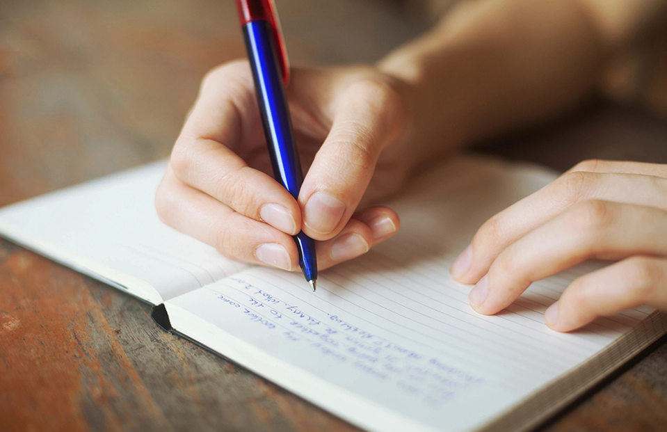 A person writing on top of a notebook.